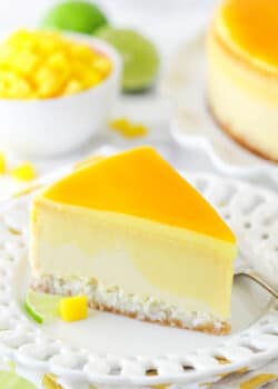 slice of mango key lime cheesecake on white plate with mango and limes in the background