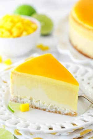 slice of mango key lime cheesecake on white plate with mango and limes in the background
