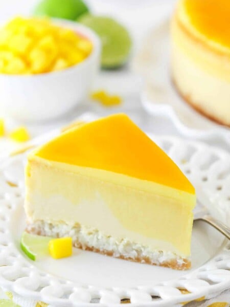 slice of mango key lime cheesecake on white plate with mango and limes in the background