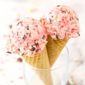 Two scoops of peppermint bark ice cream in cones propped up inside a glass.