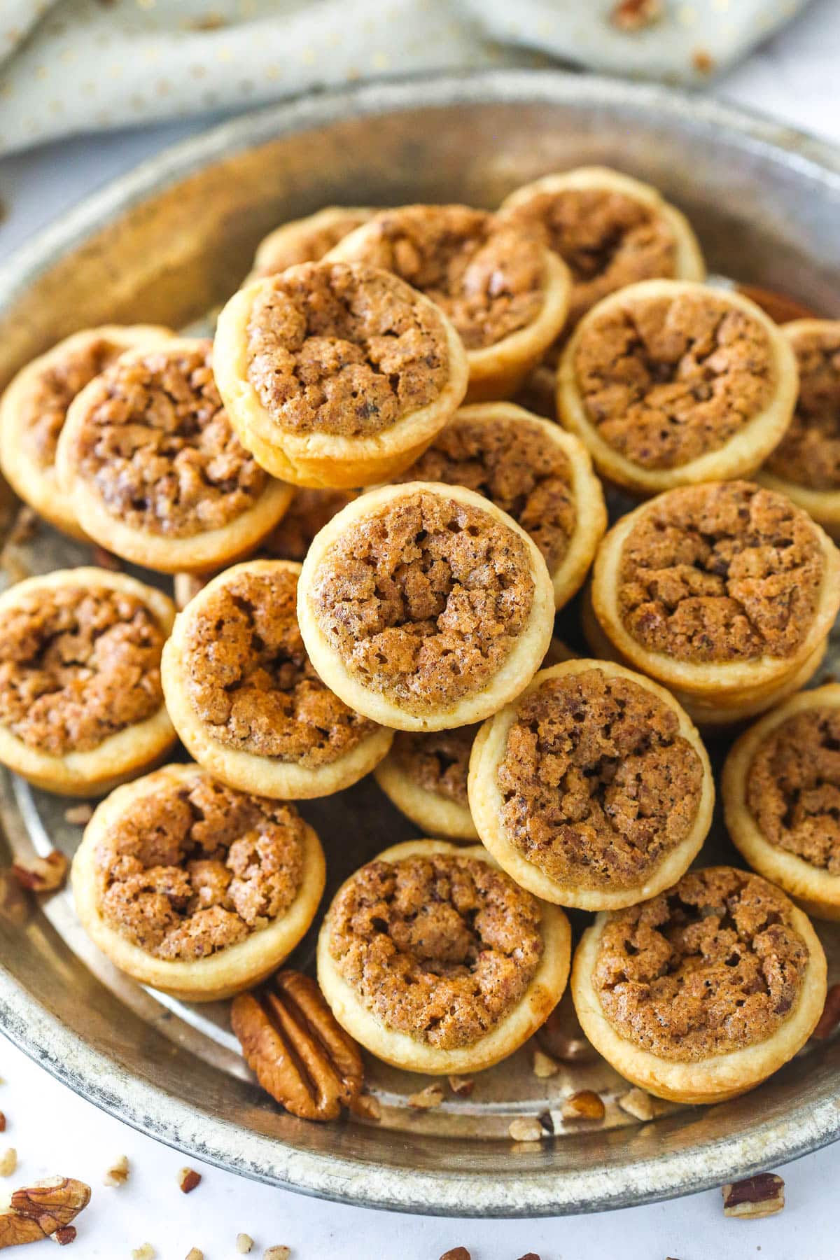 Pecan Tassies combine a cream cheese crust and decadent pecan pie filling to make for an irresistible one-bite dessert. Perect for Christmas! A metal serving tray full of pecan tassies