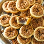 A metal tray full of pecan tassies with a bite missing from the top one.