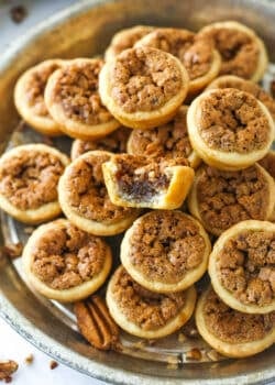 A metal tray full of pecan tassies with a bite missing from the top one.