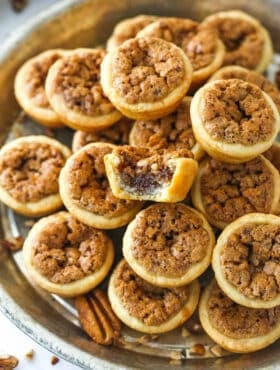 A metal tray full of pecan tassies with a bite missing from the top one.