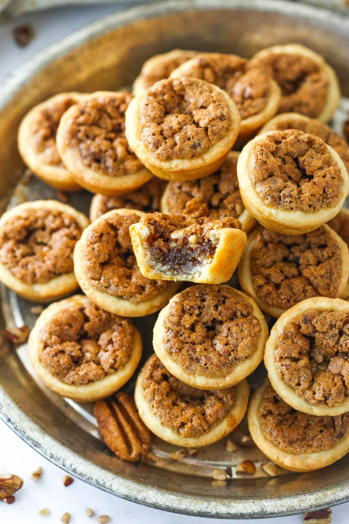 A metal tray full of pecan tassies with a bite missing from the top one.