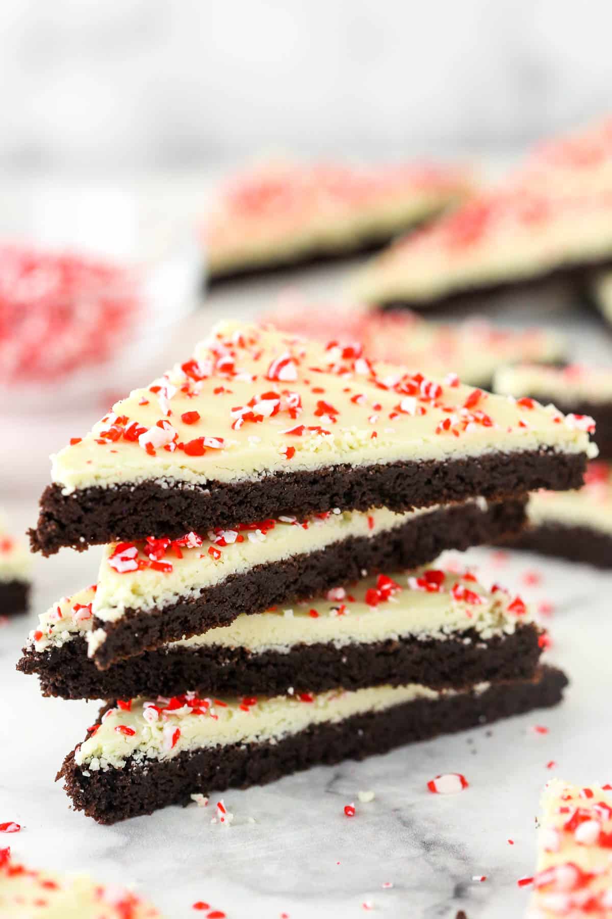 These peppermint bark cookies are made with a soft chocolate cookie base, a smooth white chocolate topping, and crushed candy canes! Festive peppermint bark cookies in a stack.