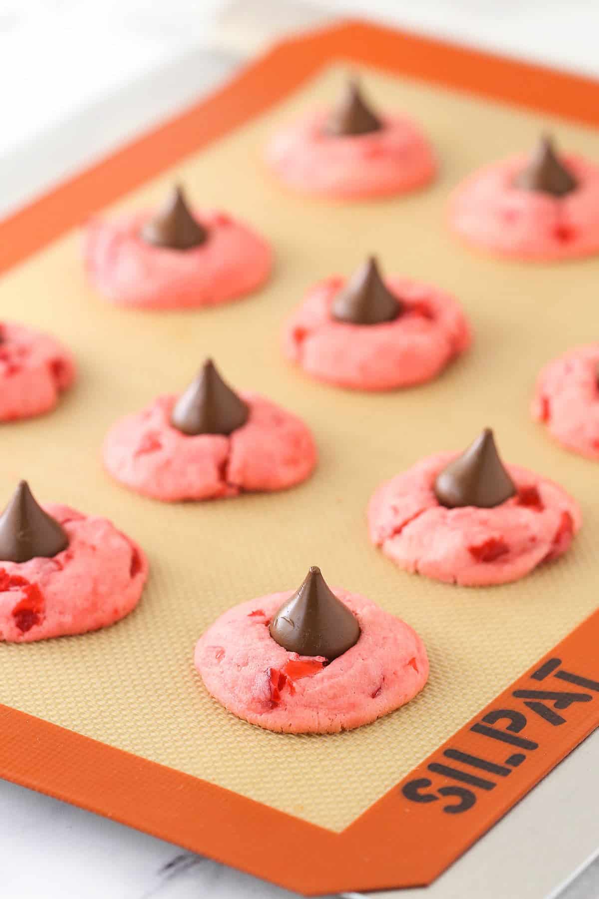 Wonderfully cute, these cherry chocolate kiss cookies are the perfect holiday treat. The secret to their flavor? Cherry juice. Cherry kiss cookies on a silicone baking sheet.