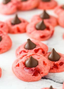 Lots of cherry kiss cookies on a flat surface.