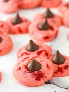 Lots of cherry kiss cookies on a flat surface.