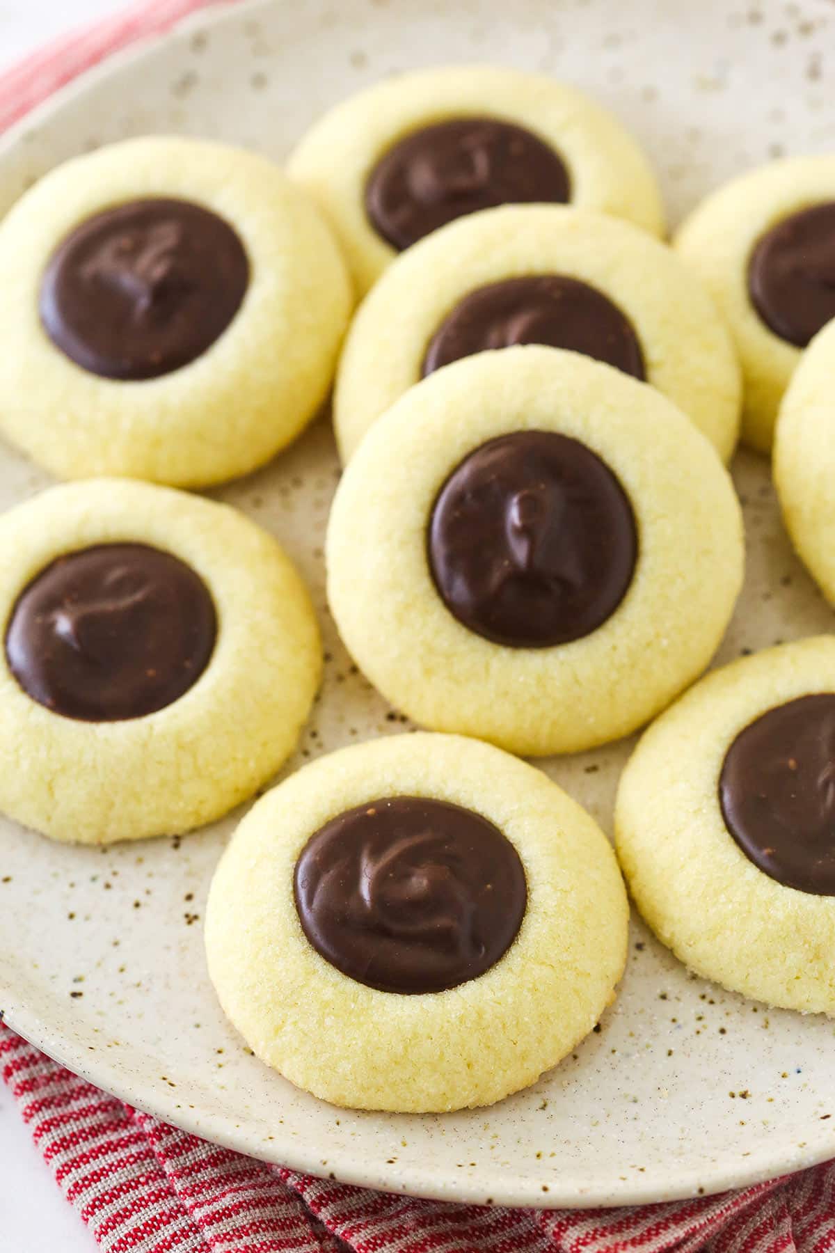 Chocolate thumbprint cookies on a speckled plate and red striped napkin.