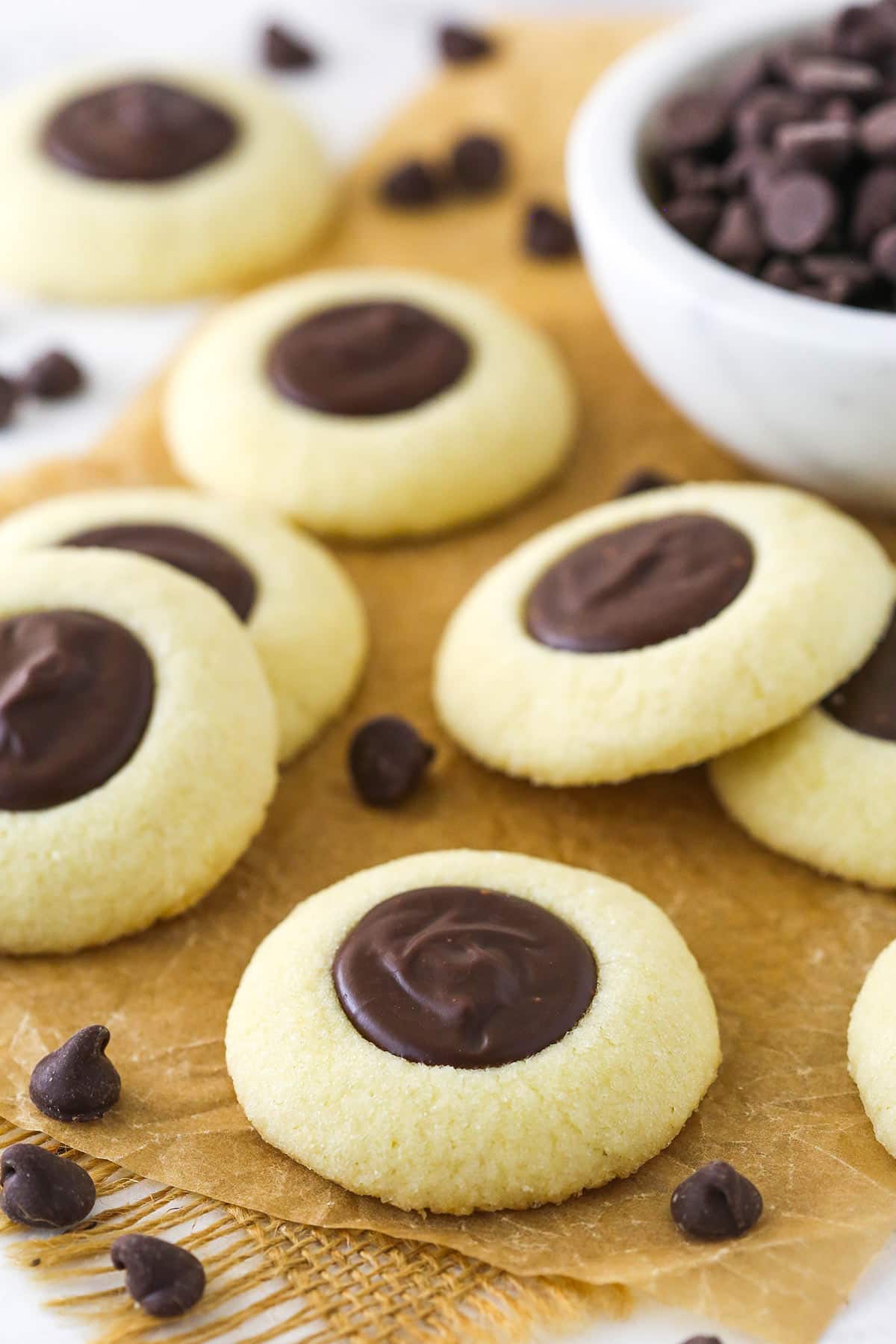 These addictive chocolate thumbprint cookies are made with a vanilla shortbread-like base and a silky chocolate ganache filling. Chocolate thumbprint cookies on brown parchment paper.