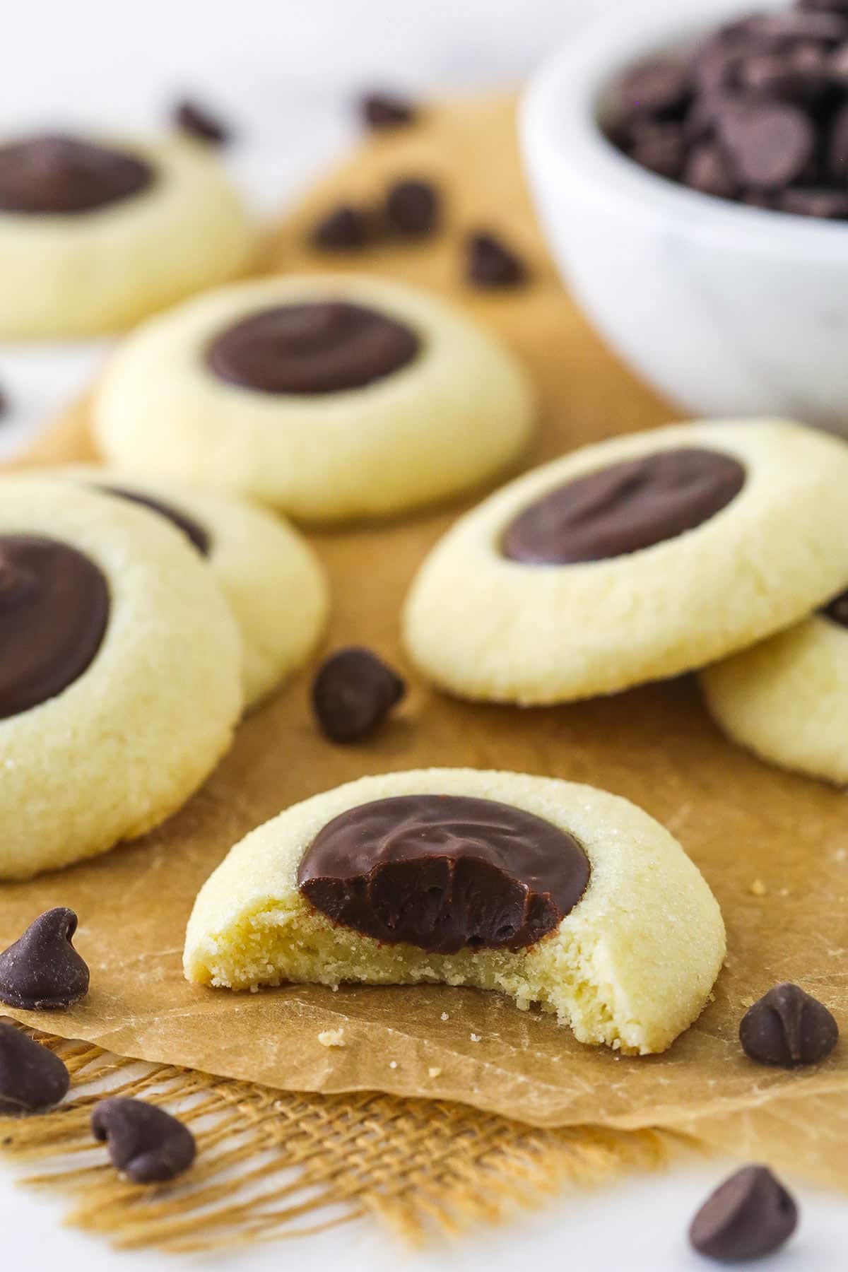 Chocolate thumbprint cookies on brown parchment paper with a bite taken out of one.