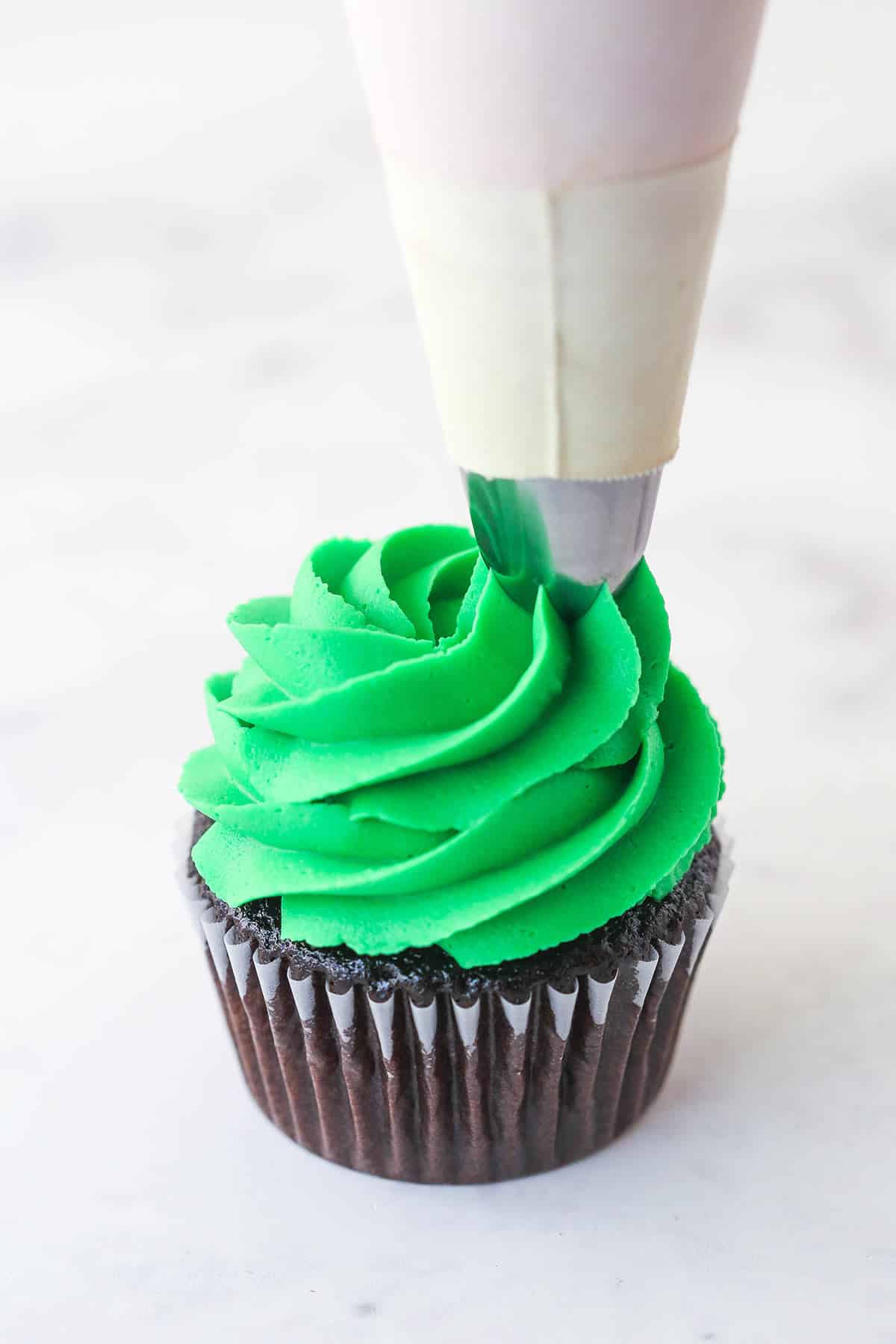 piping the green buttercream onto the cupcake for the christmas tree cupcakes