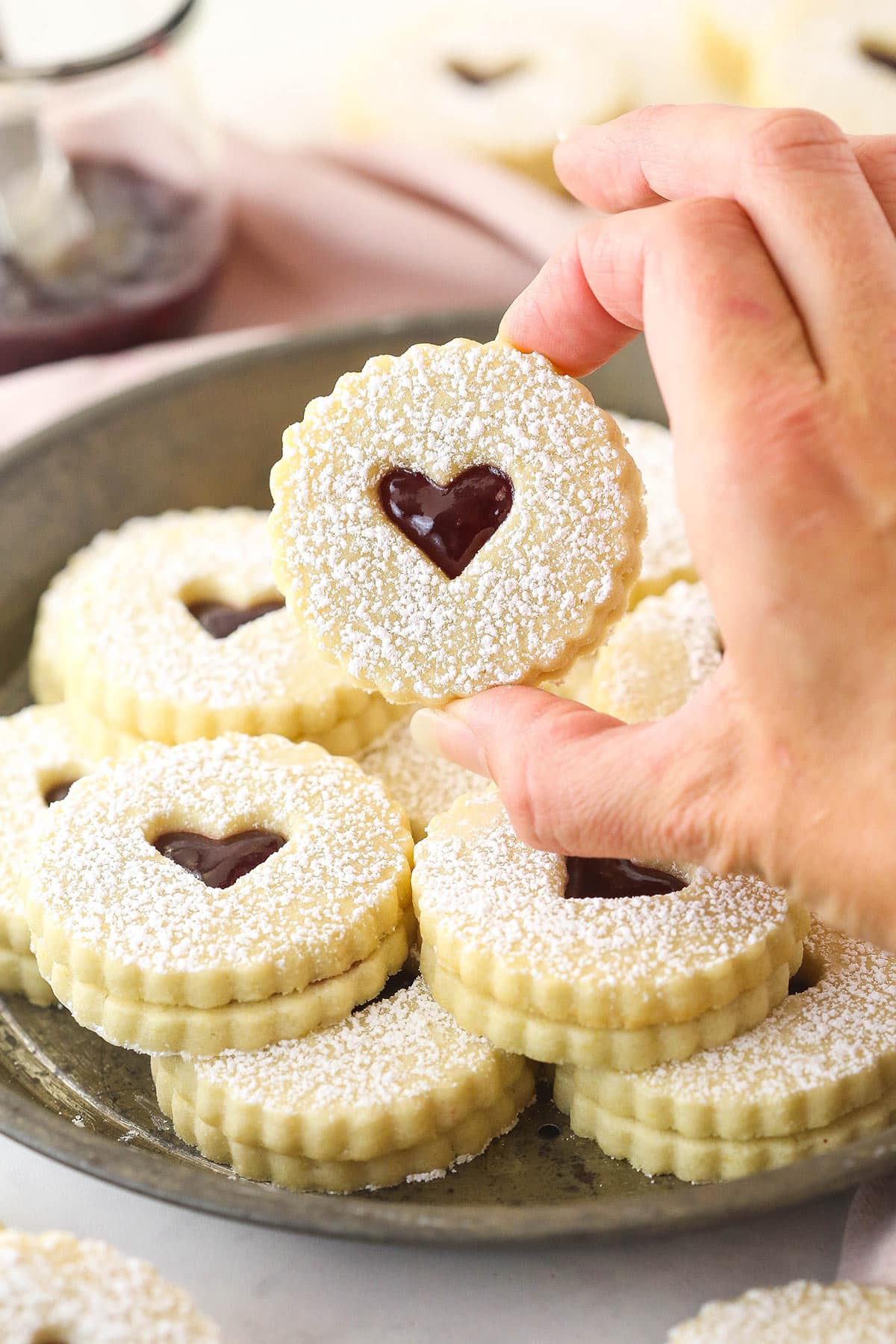 Holding up a linzer tart cookie in between two fingers.