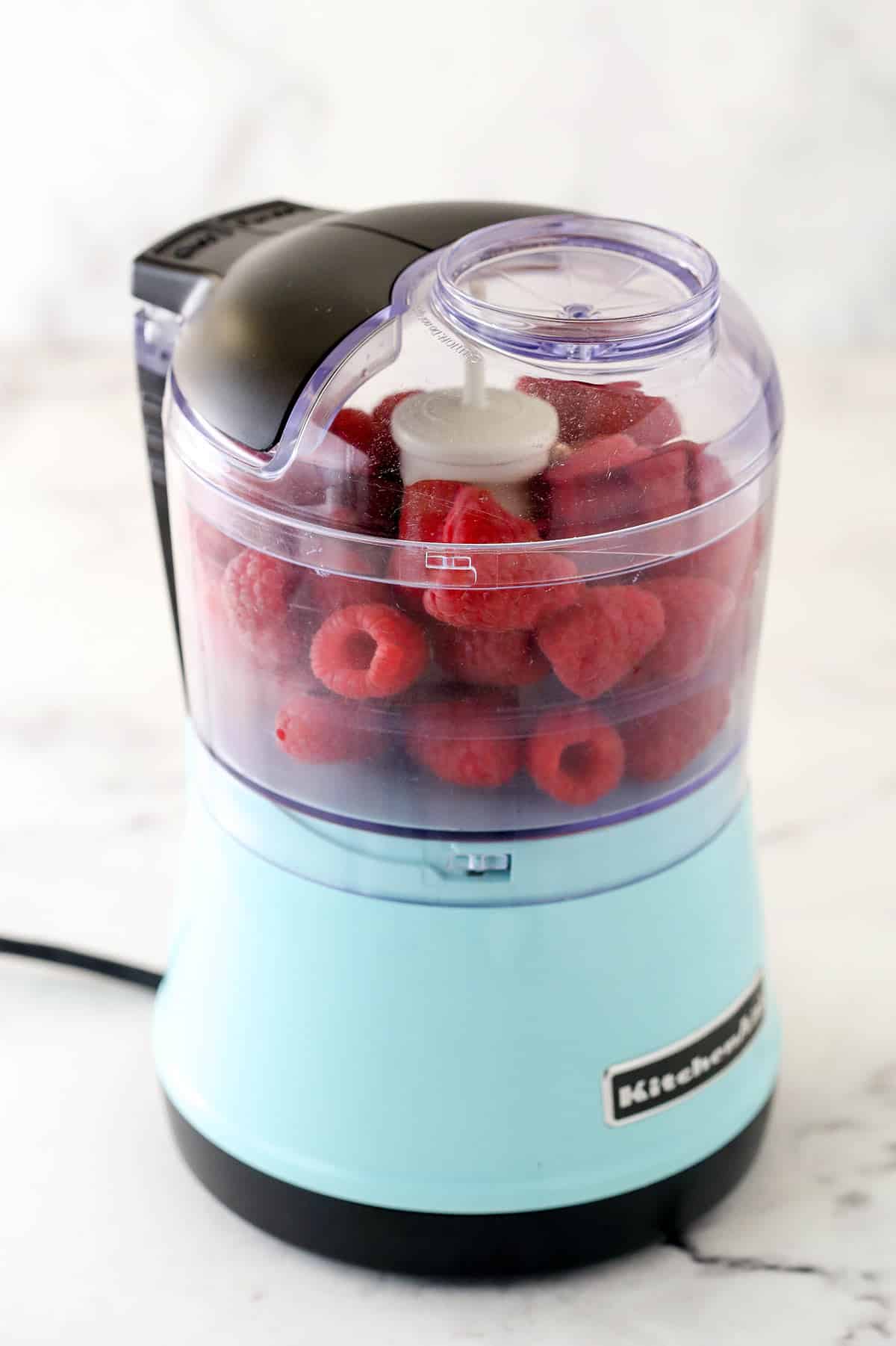Bright pink and fruity, this raspberry filling for cake will give all your baked goods a pop of color and a burst of flavor. Adding the raspberries to the food processor.
