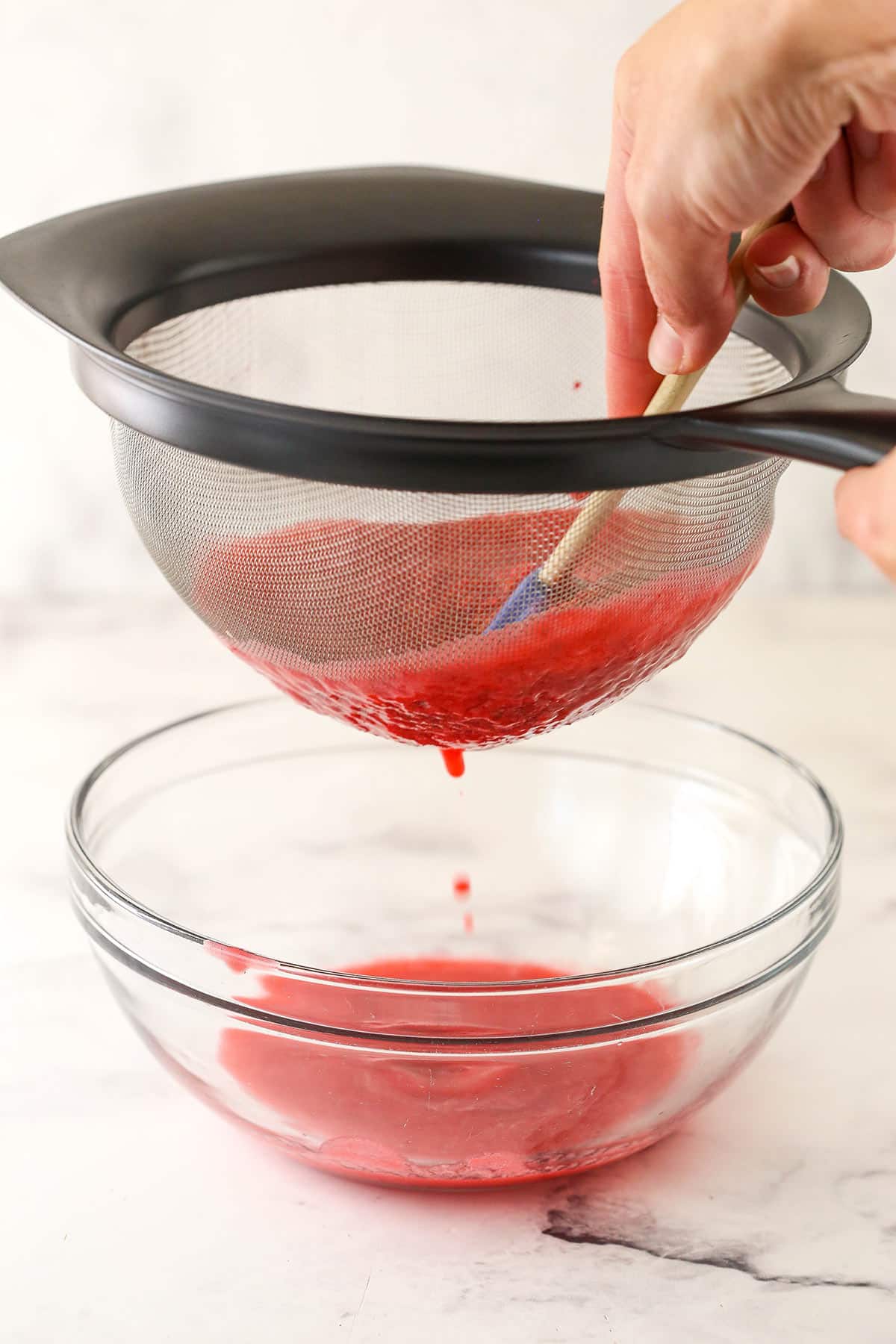 Straining the raspberry puree into a bowl.