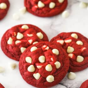 Angled shot of three red velvet cookies with white chocolate chips, with more cookies in the background.