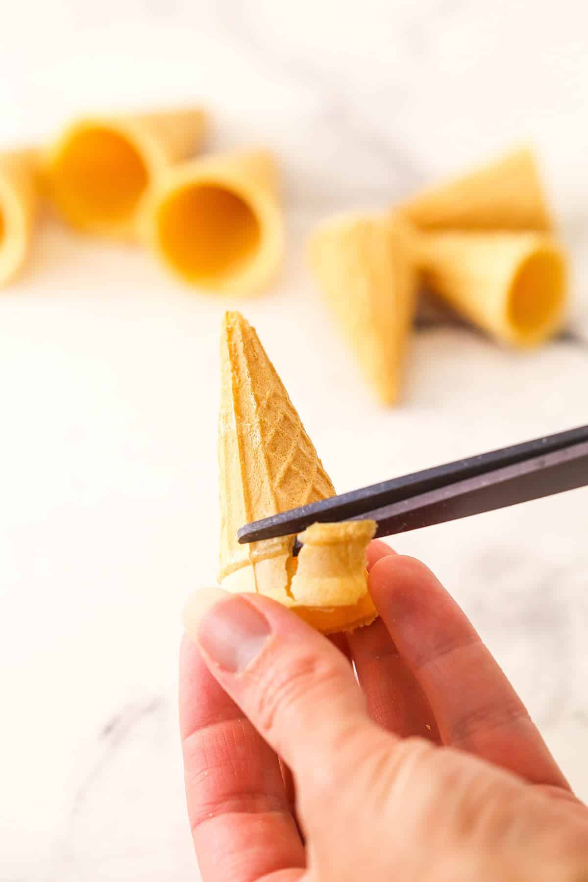 Snipping off the whole pointy end from the ice cream cone with scissors.