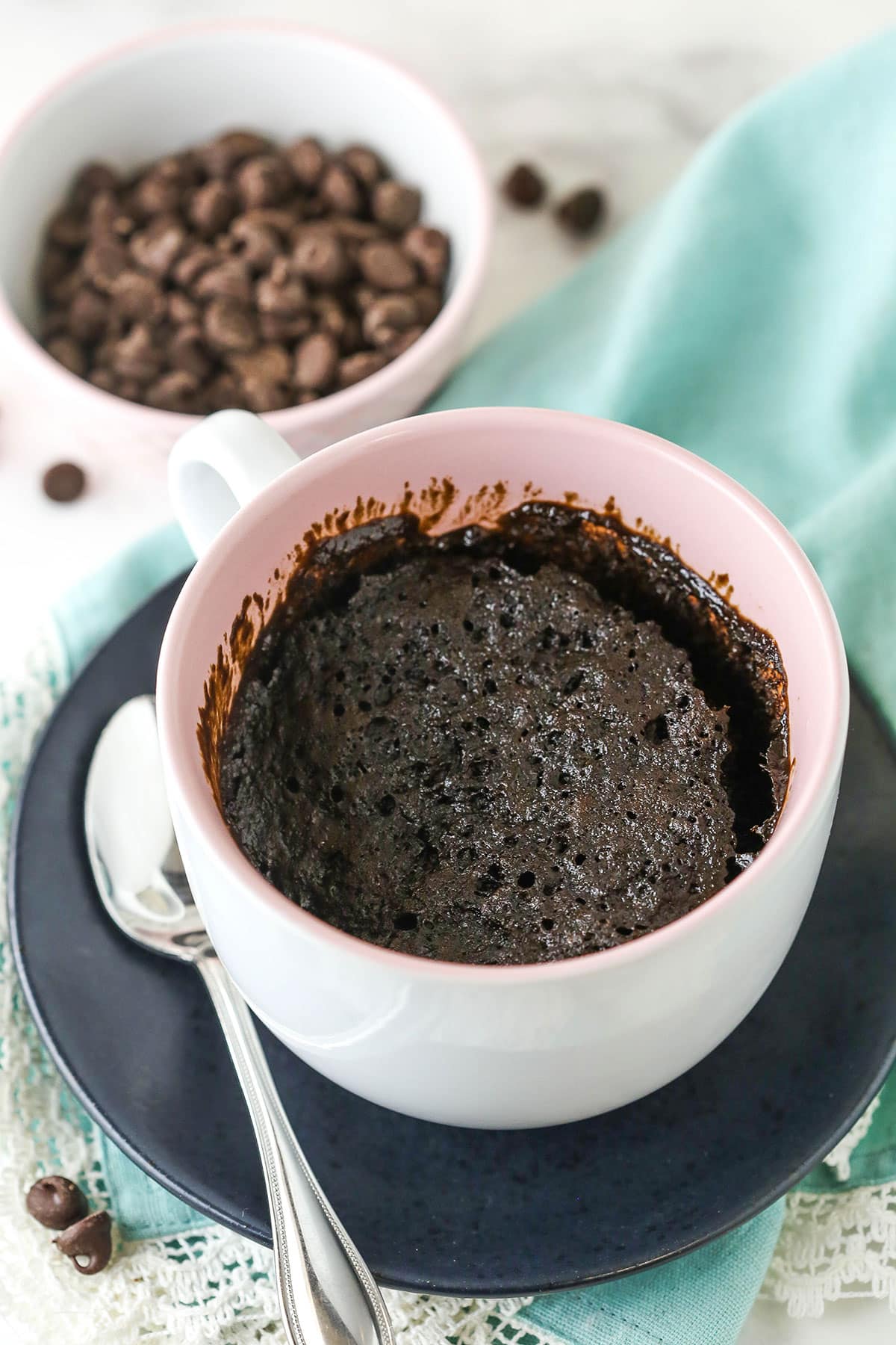 A Chocolate Mug Cake in a pink bowl on a black plate with a spoon