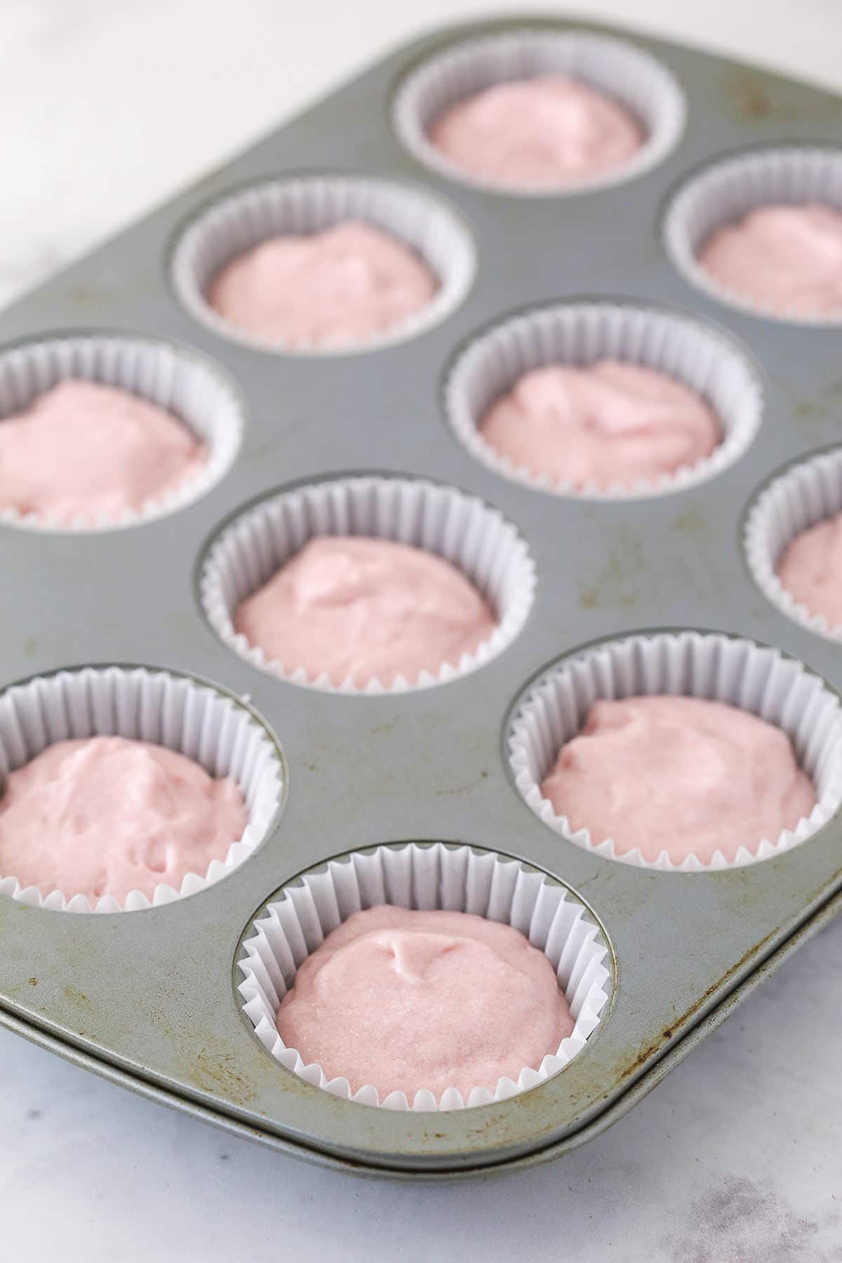 Cupcake tins with cupcake liners filled with batter for conversation heart cupcakes.