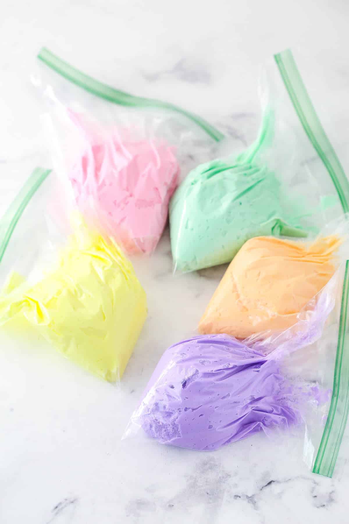 Ziplock bags full of different colors of buttercream frosting for rainbow frosting to top conversation heart cupcakes.