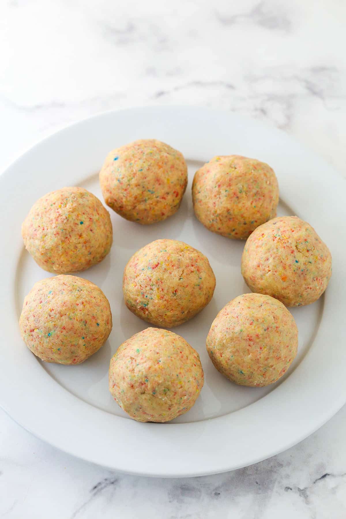 Dough for Fruity Pebbles cookies rolled into balls and arranged on a plate.