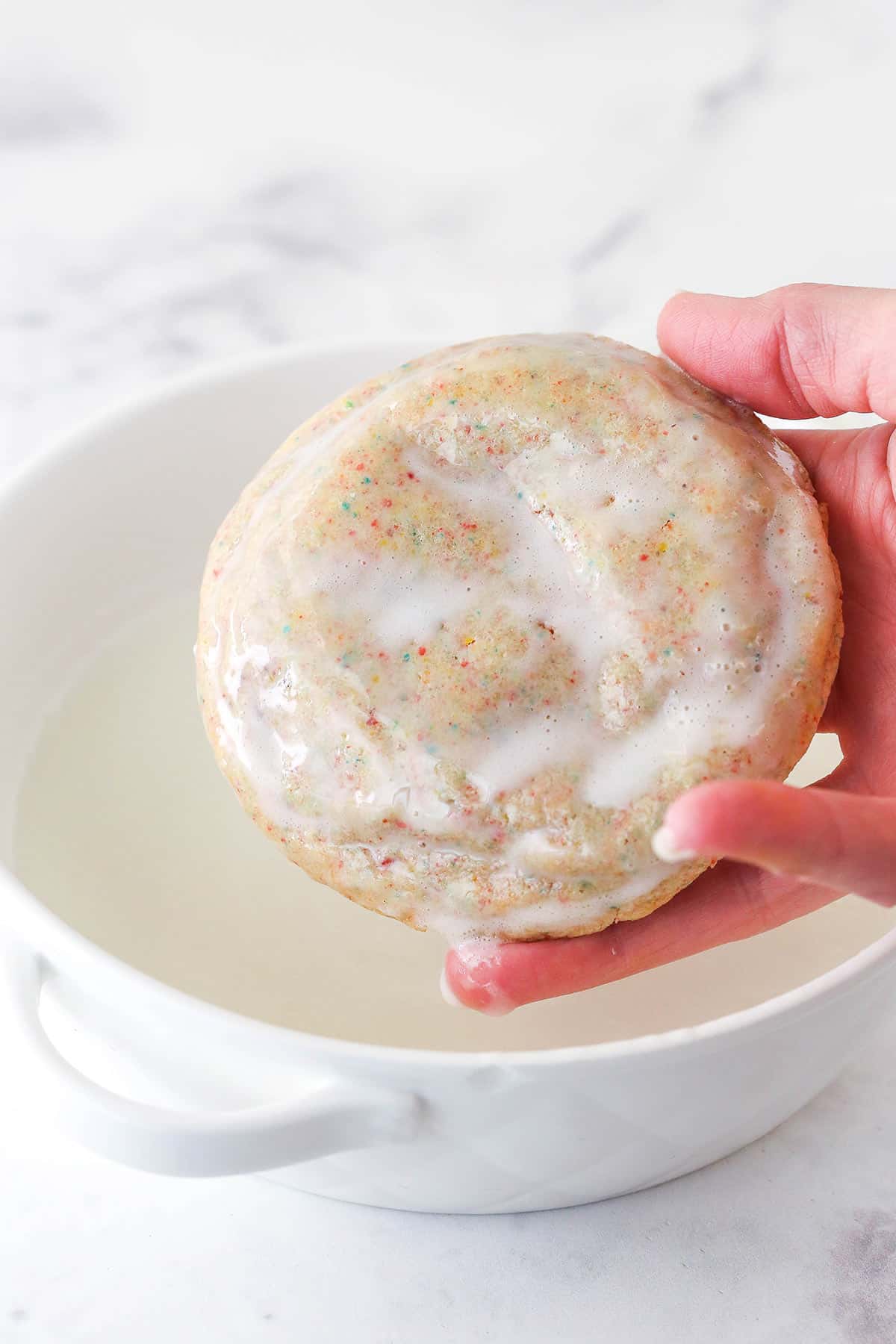 Dipping a Fruity Pebbles cookie in a bowl of glaze.