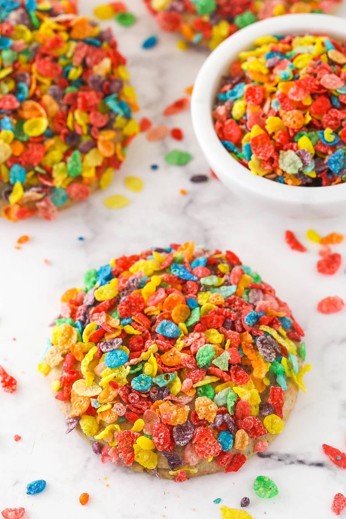 Fruity Pebbles cookies on a counter near a bowl of Fruity Pebbles.