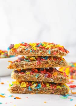 A stack of Fruity Pebbles cookies near a bowl of Fruity Pebbles.