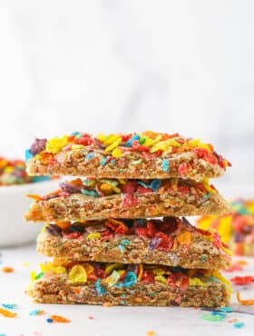 A stack of Fruity Pebbles cookies near a bowl of Fruity Pebbles.
