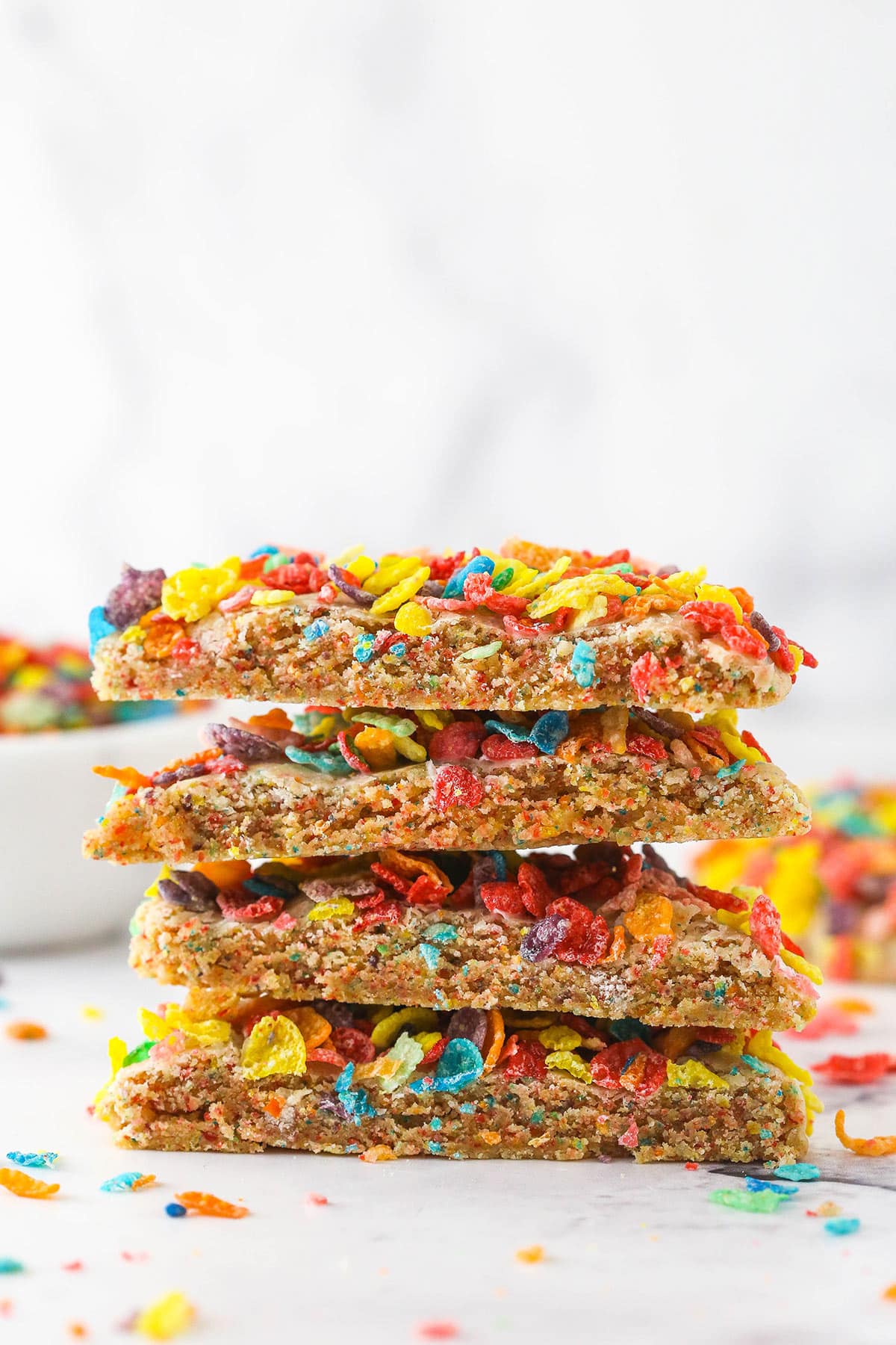 A stack of Fruity Pebbles cookies near a bowl of Fruity Pebbles.