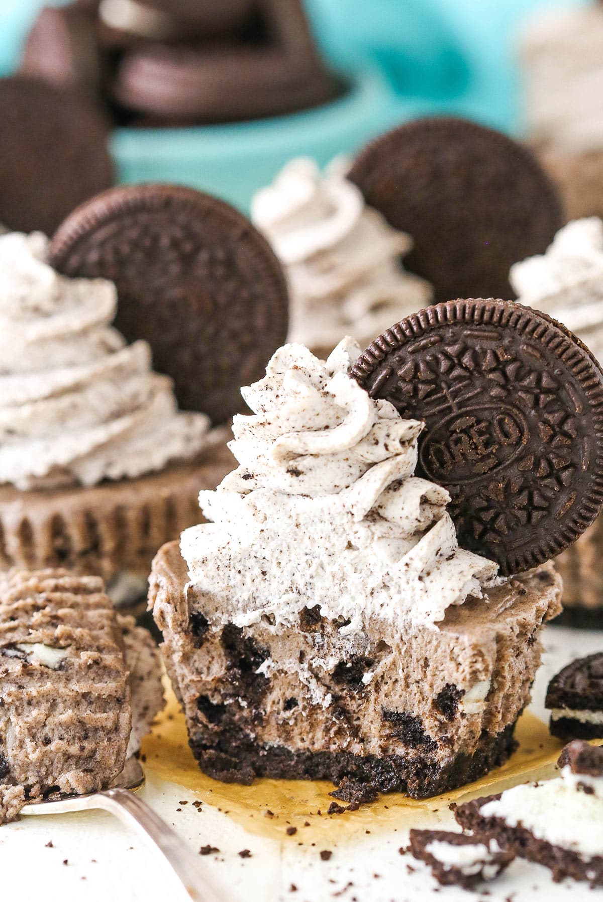 A no bake mini Oreo cheesecakes with a bite taken out of it surrounded by other no bake mini Oreo cheesecakes near a bowl of Oreos.