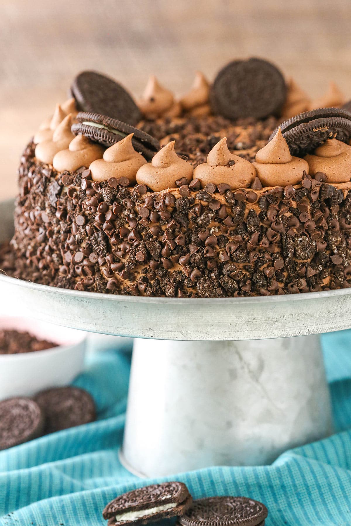 A whole Ultimate Oreo cheesecake on a serving platter with Oreo cookies scatter below.