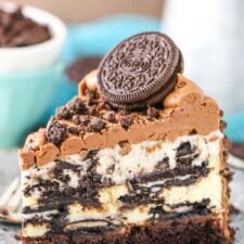 A slice of layered Oreo cheesecake topped with chocolate frosting and Oreo cookies on a plate.