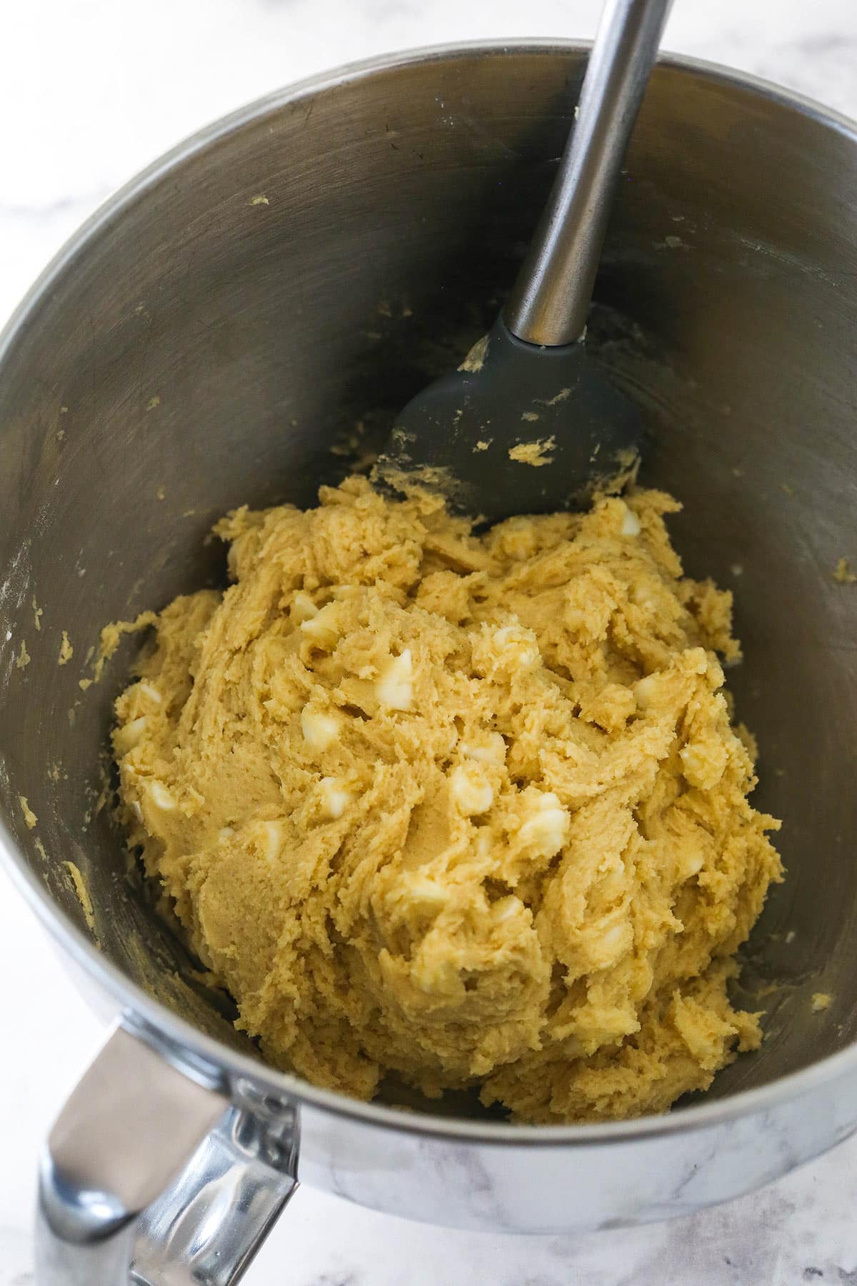 Cookie dough in the bowl of a standup mixer with white chocolate chips for white chocolate chip cookies.