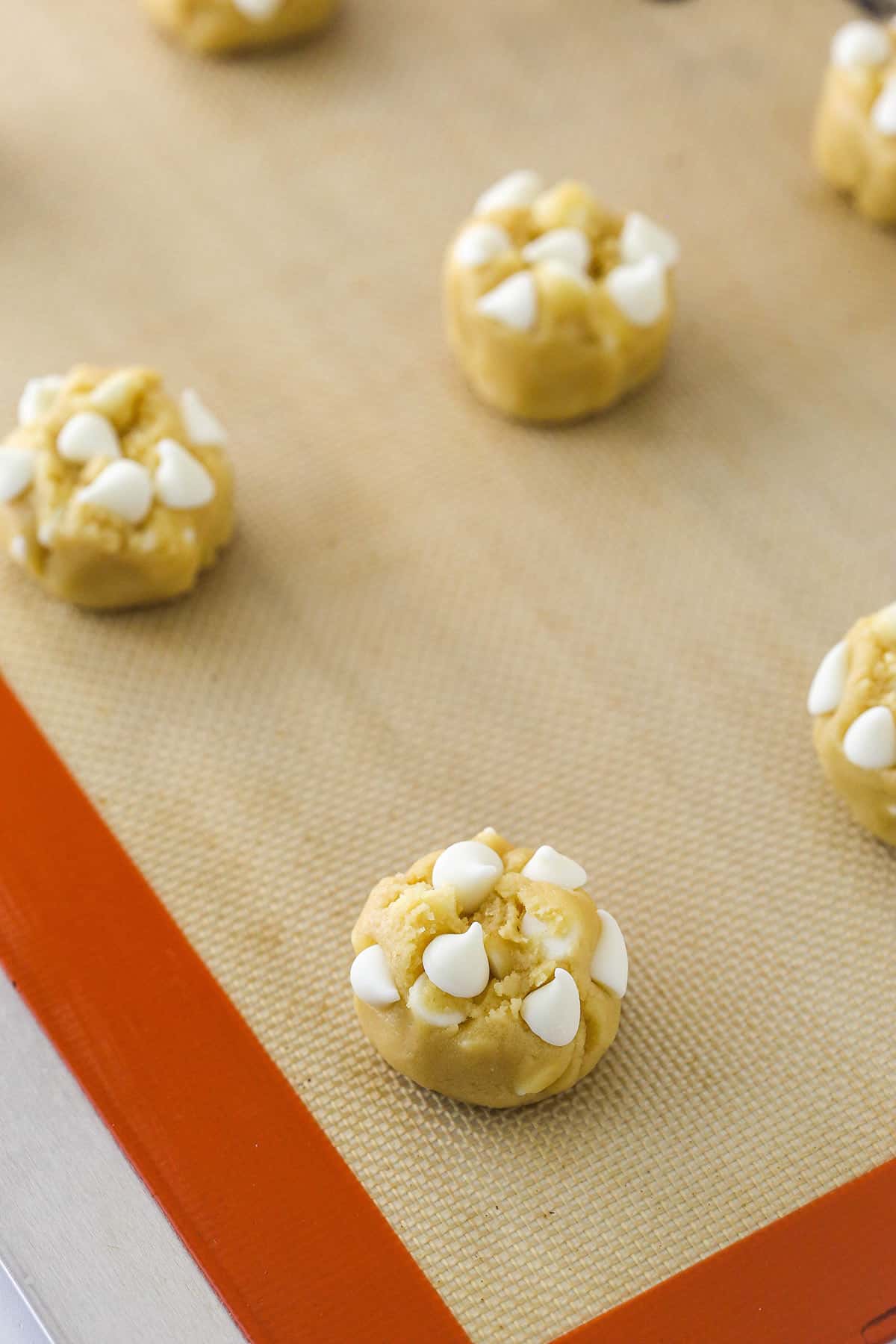 White chocolate chip cookie dough on a baking mat on a cookie sheet ready to be baked.