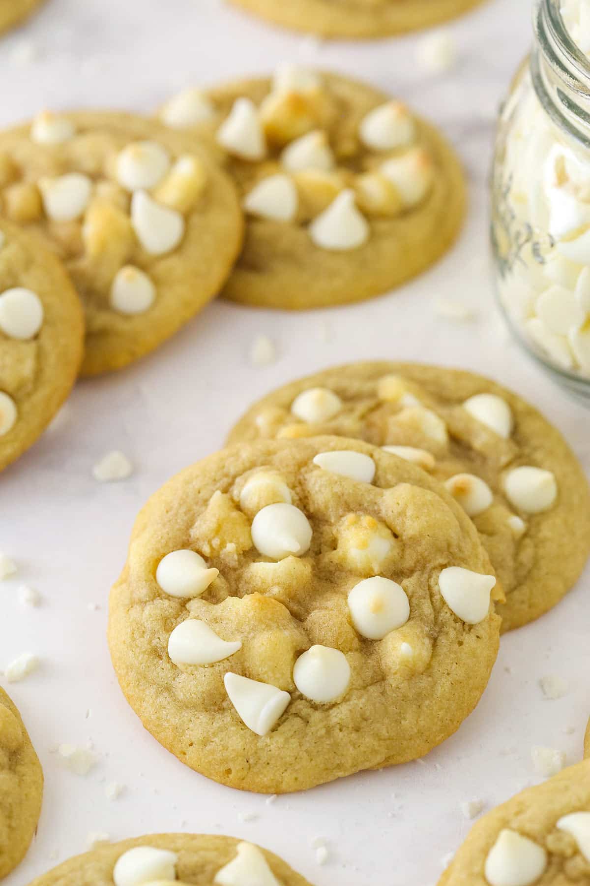 White chocolate chip cookies fanned on top of one another near a jar of white chocolate chips.