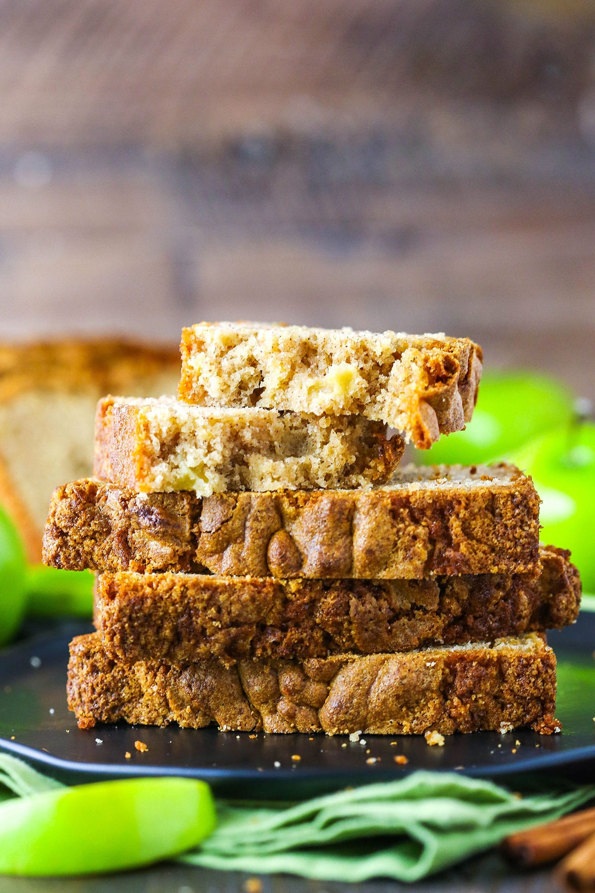 Four slices of Apple Bread stacked with the top slice broken in two pieces, on a black plate