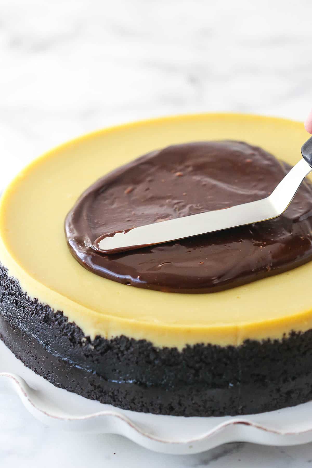 Spreading chocolate ganache over a cheesecake.