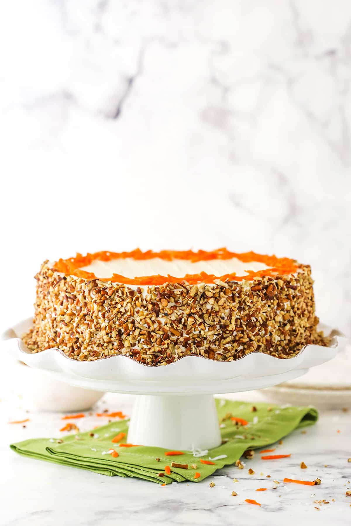 Side view of a full Cheesecake Swirl Carrot Cake on a white cake stand