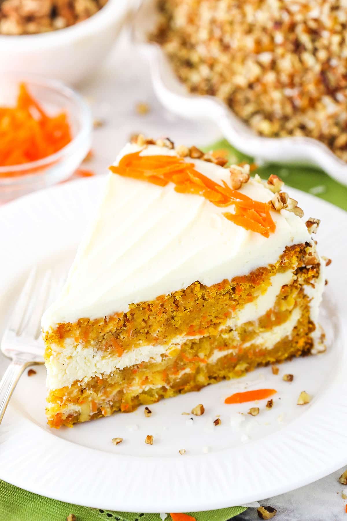 A slice of Cheesecake Swirl Carrot Cake on a white plate with a fork