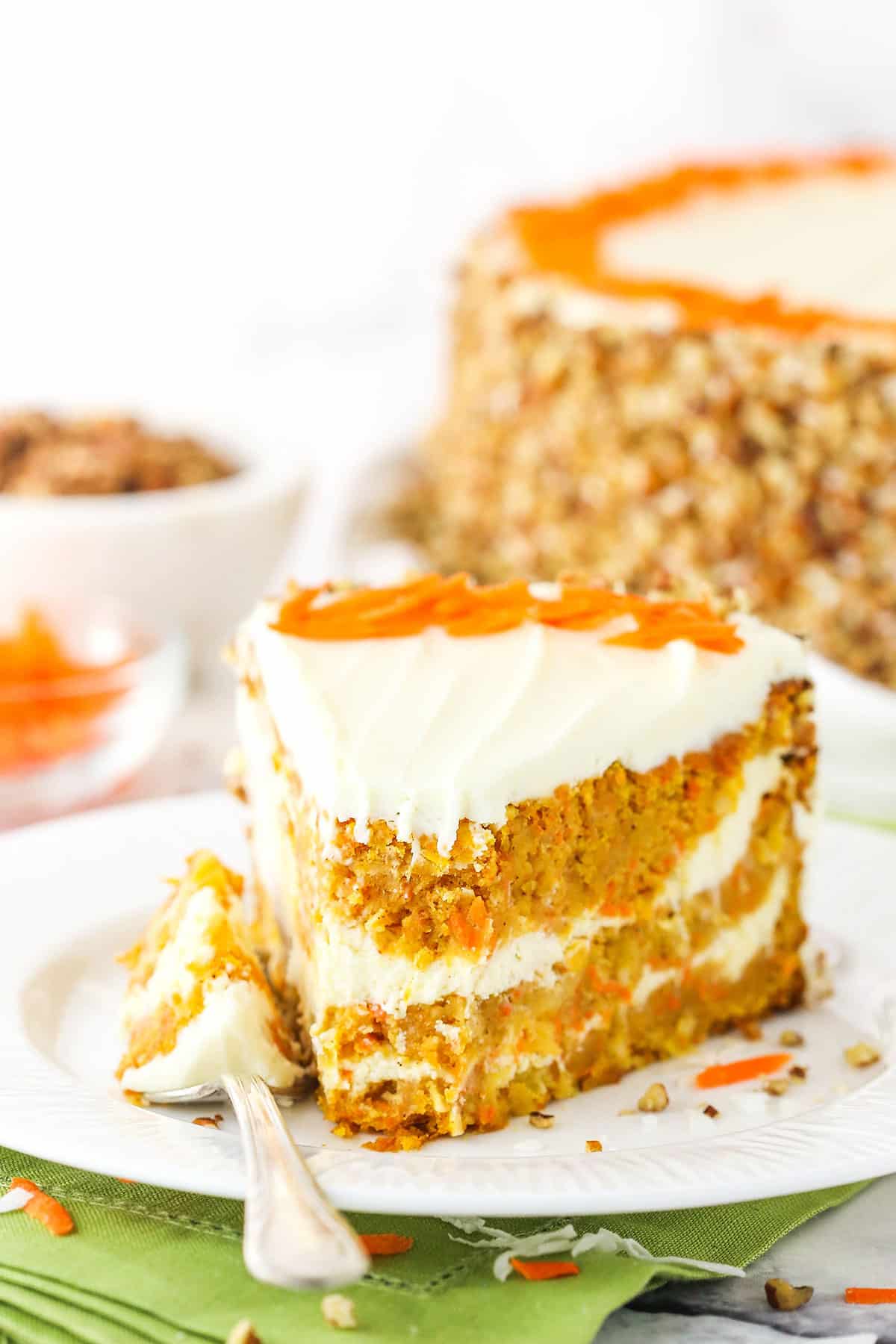 A slice of Cheesecake Swirl Carrot Cake with a bite taken out on a white plate with a fork