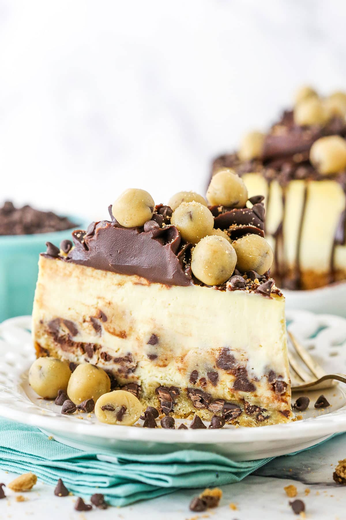This Chocolate Chip Cookie Dough Cheesecake is made with a chocolate chip cookie crust and brown sugar cheesecake filled with chocolate chips and cookie dough! It's topped with chocolate ganache and more cookie dough for the ultimate treat! side image of cookie dough cheesecake slice