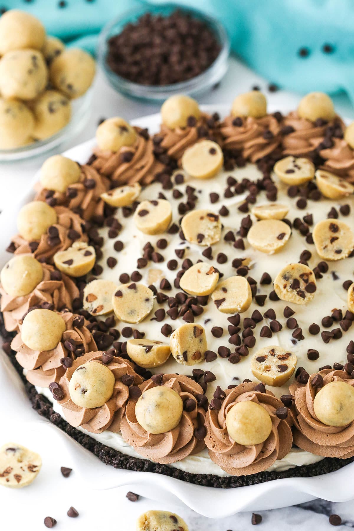 Overhead view of a full Chocolate Chip Cookie Dough Ice Cream Pie in a white platter with cookie dough balls and chocolate chips in the background