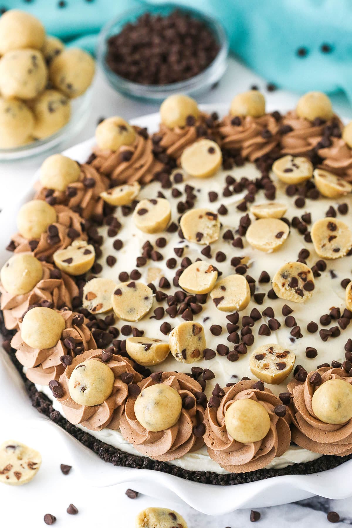 Overhead view of a full Chocolate Chip Cookie Dough Ice Cream Pie in a white platter with cookie dough balls and chocolate chips in the background