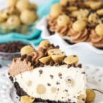 Slice of Chocolate Chip Cookie Dough Ice Cream Pie on a white plate with a fork and cookie dough balls and chocolate chips in the background