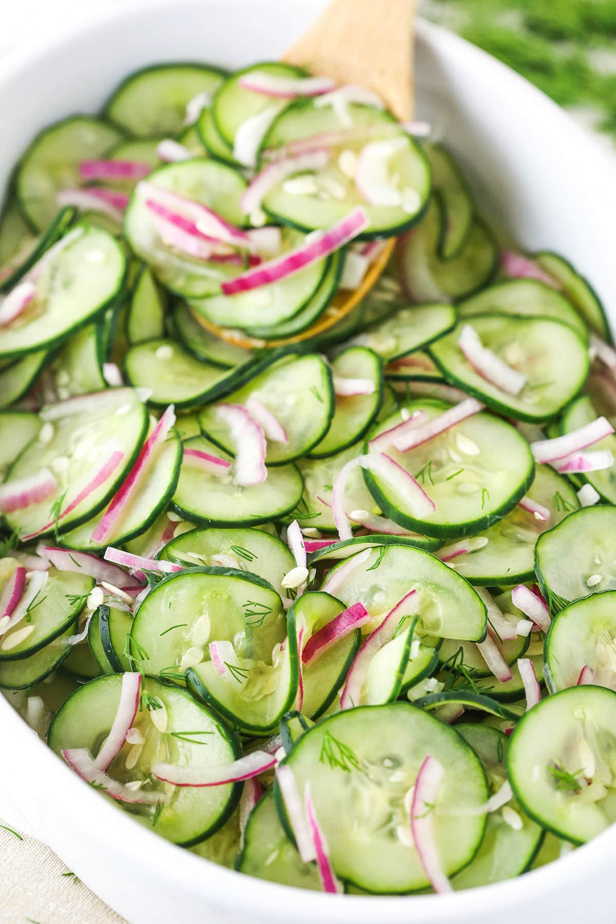 close up of cucumber salad in a white dish with a wooden spoon