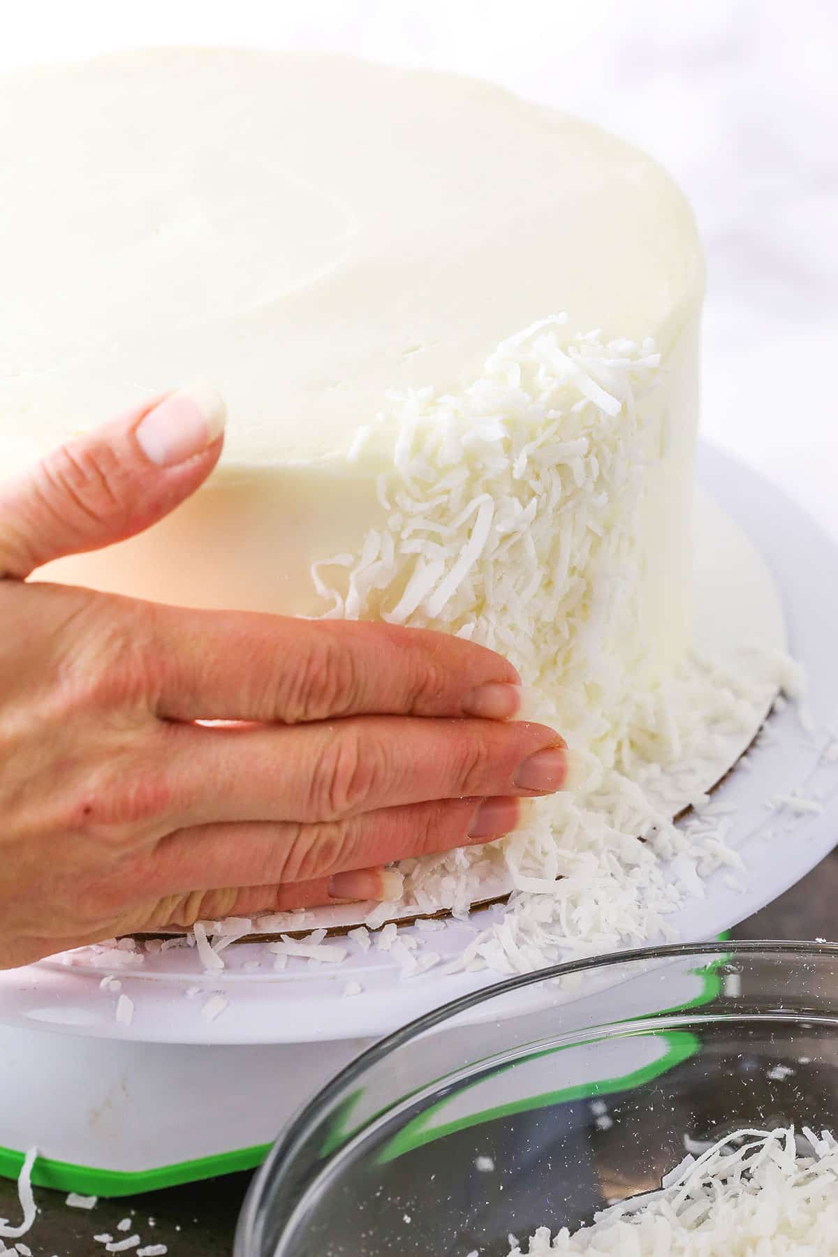 Step of making Easter Bunny Cake showing using my hand to press the coconut shavings onto the side of the cake.