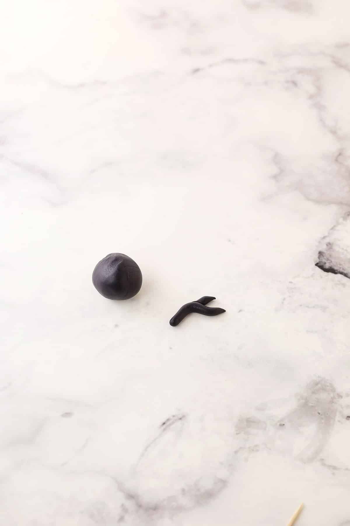 Step 2 of making fondant bunny eyes and nose showing taking a second piece of black fondant and rolling it and shaping it to make it look like the eye.