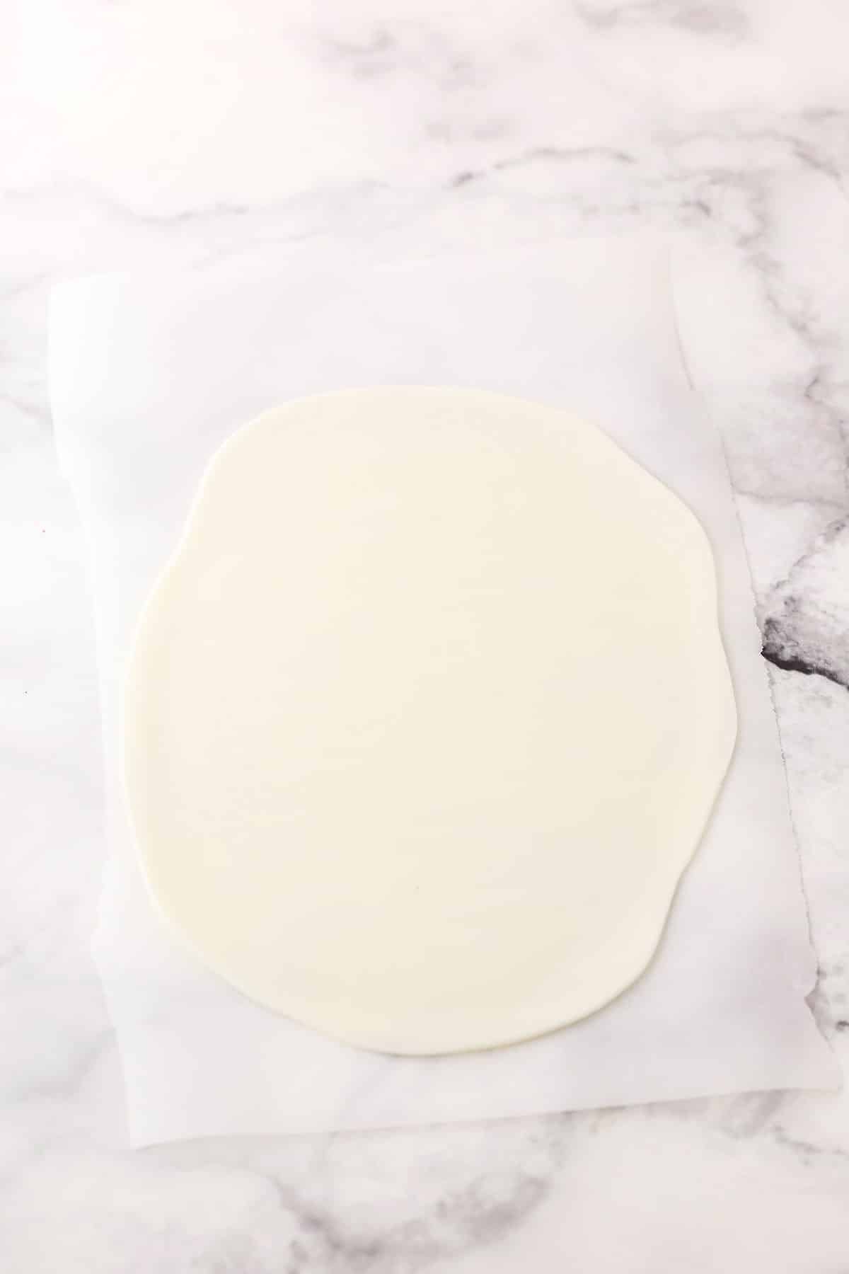 Step 1 of making fondant bunny ears showing rolling out white fondant flat on a table top